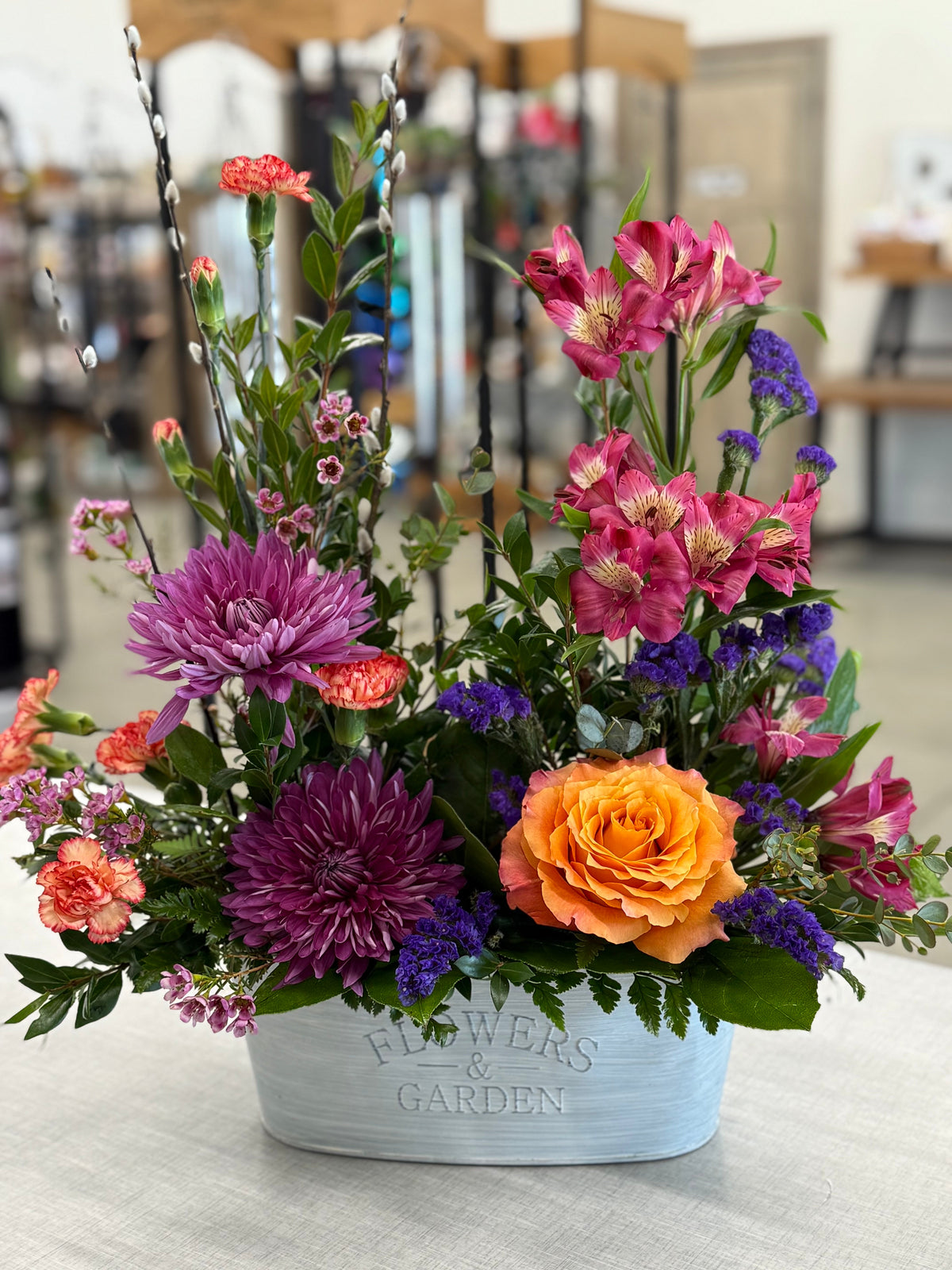 A variety of fresh cut flowers arranged into a beautiful bouquet with a blue and white container labeled 'GARDEN'.