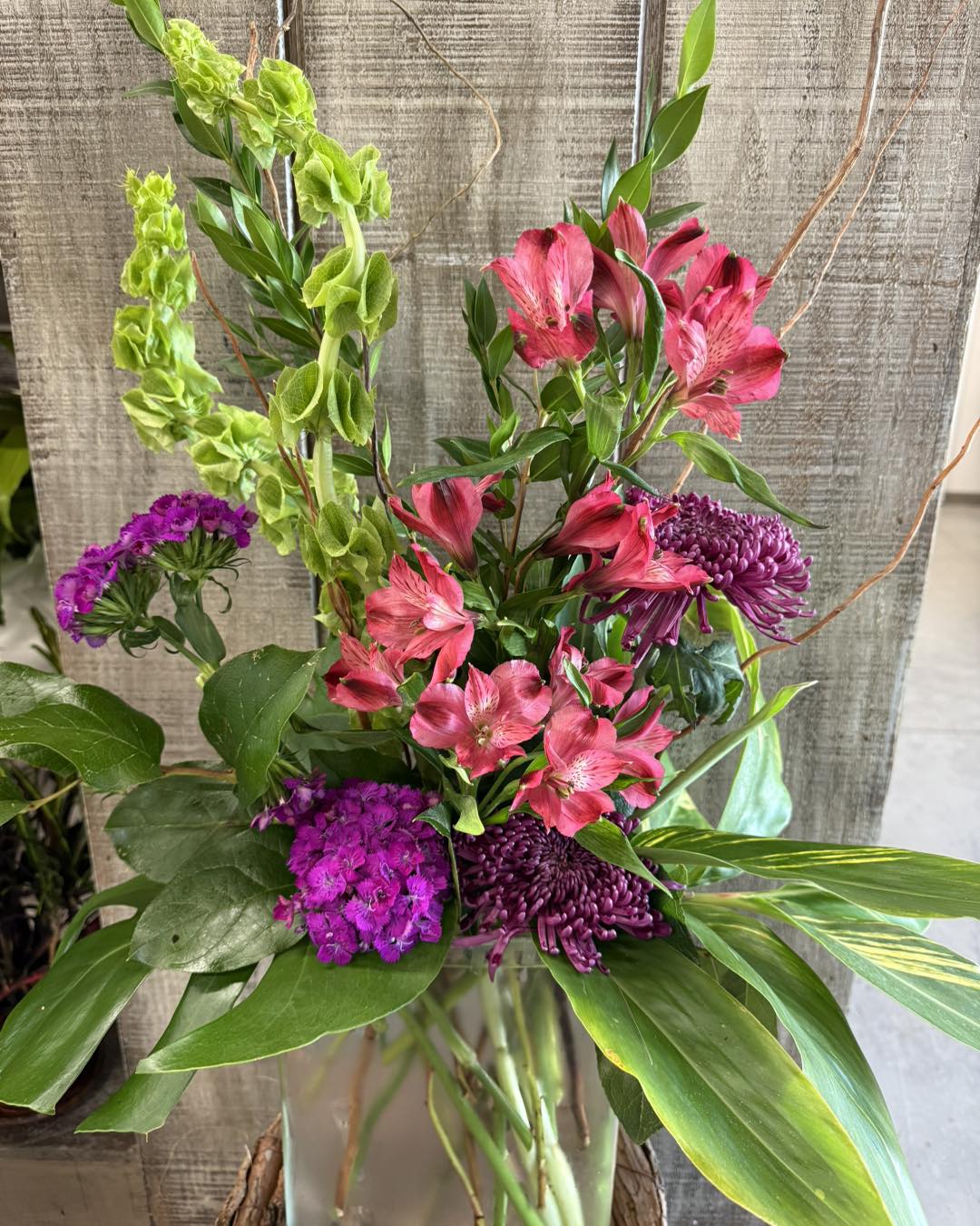 Bouquet of flowers with pink and purple flowers against a textured wall.
