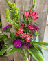 Bouquet of flowers with pink and purple flowers against a textured wall.
