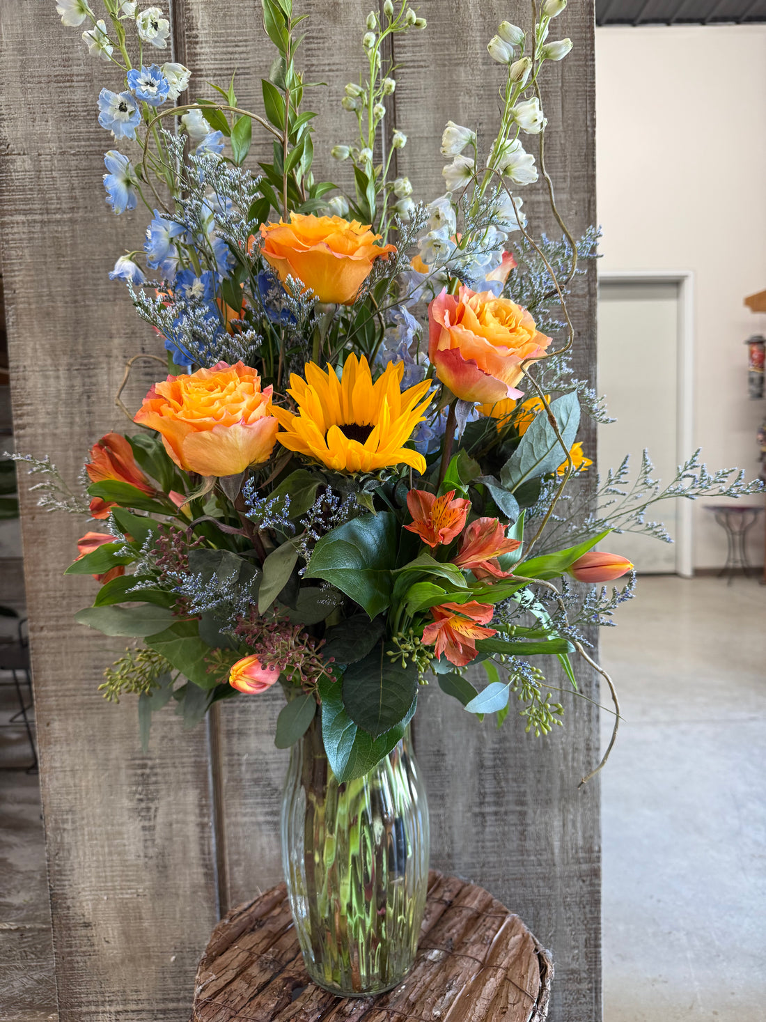 A vibrant bouquet of fresh cut flowers, featuring citrus orange, blue, and yellow colors, arranged in a clear vase.