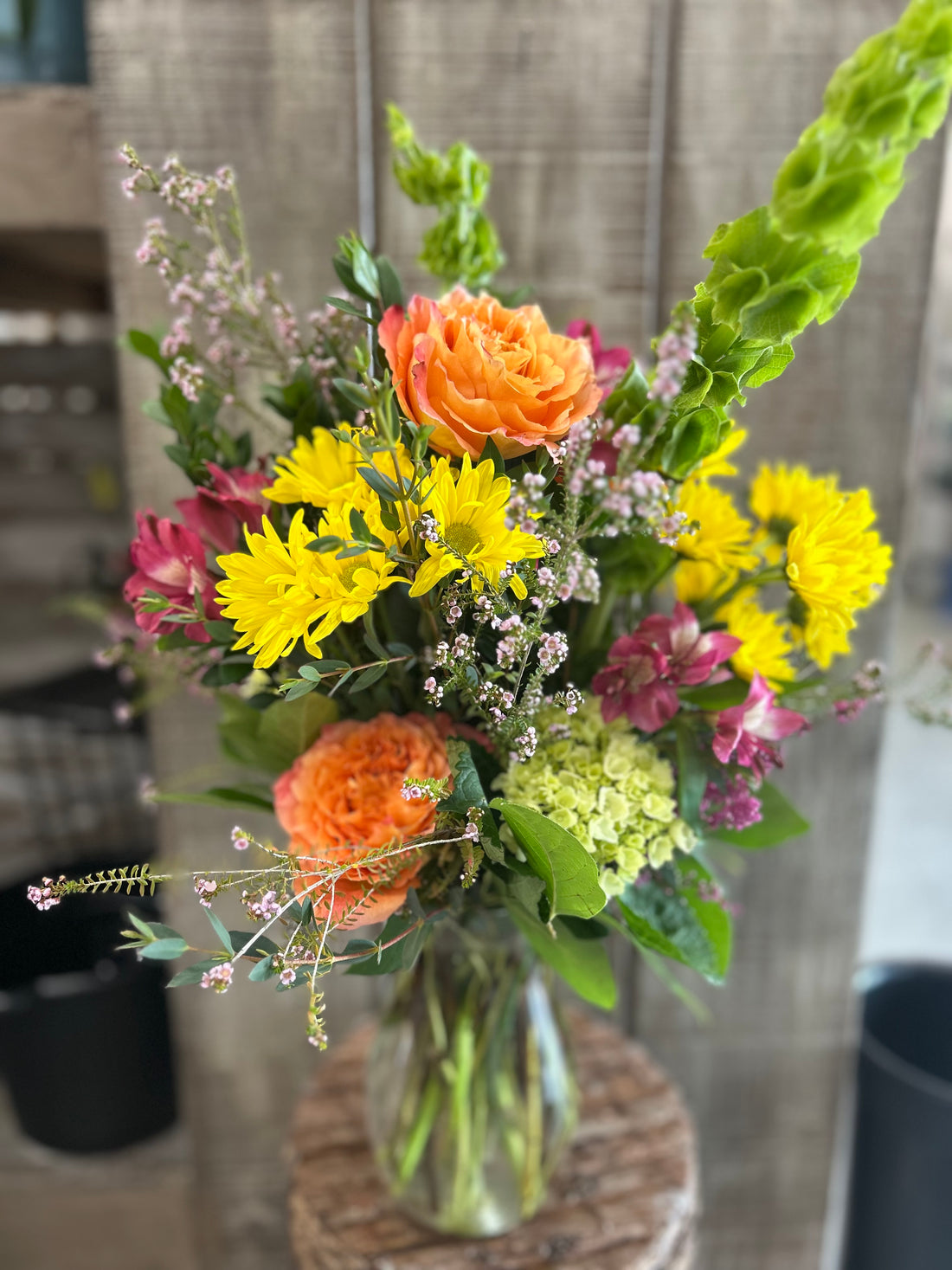 A vibrant flower bouquet featuring yellow, orange, and pink flowers with greenery, arranged in a clear vase.