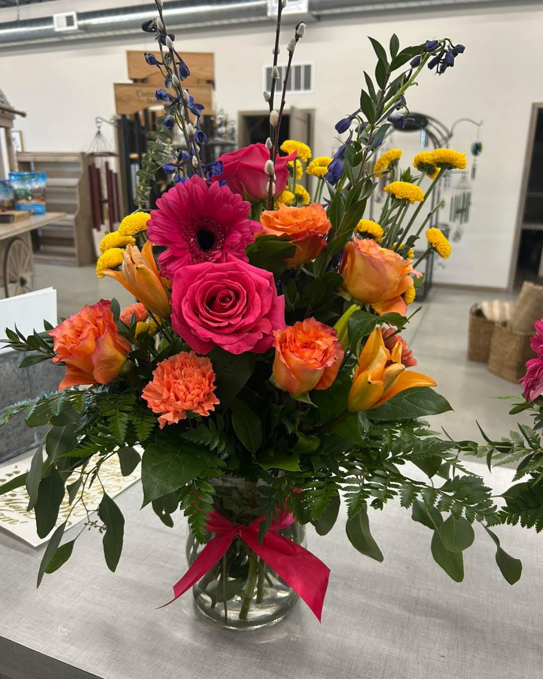 A vibrant bouquet featuring a mix of flowers including roses and other blooms in shades of pink, orange, yellow, and green, arranged in a glass vase.