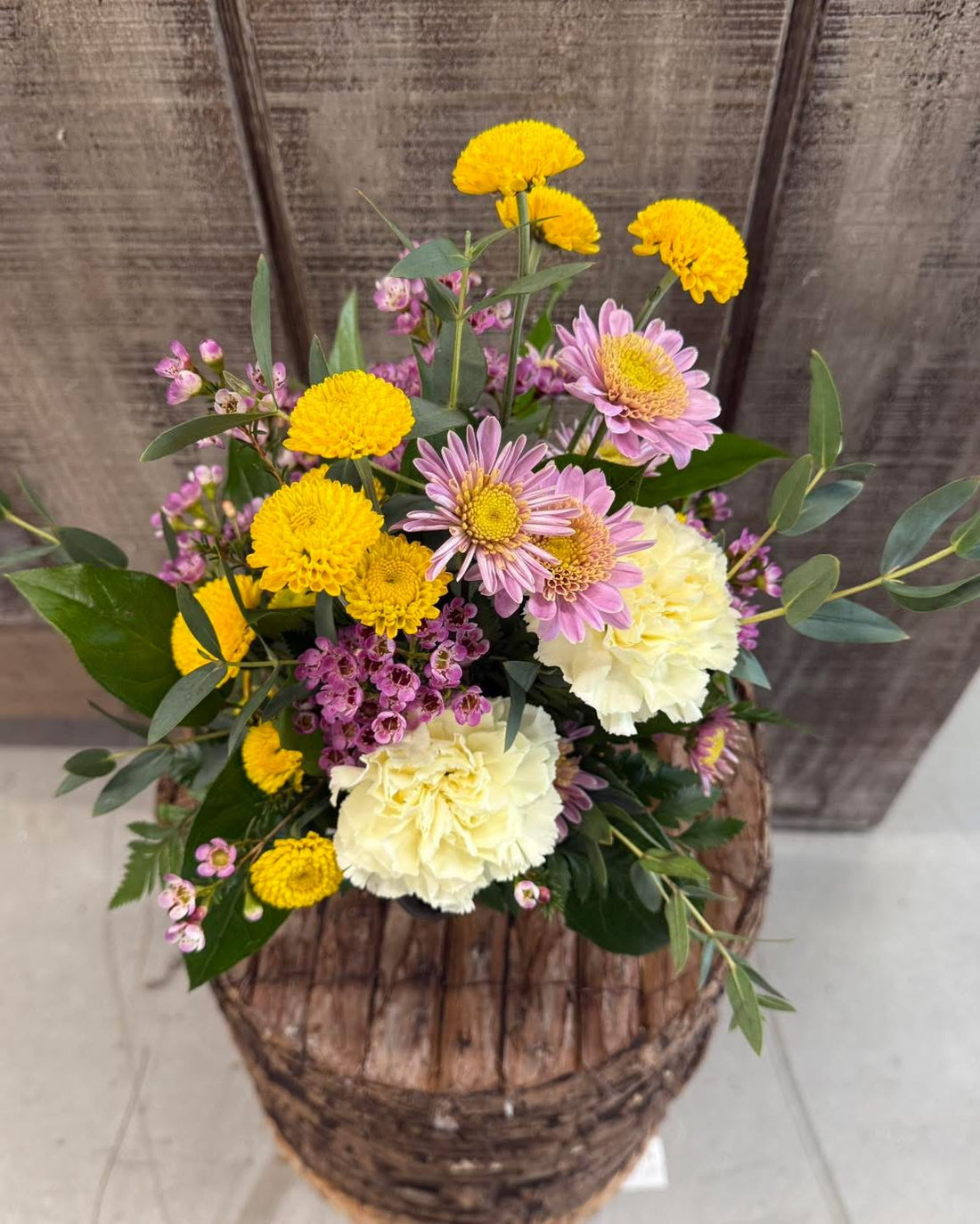 A bouquet of freshly cut flowers including yellow, pink, and white flowers with green leaves.