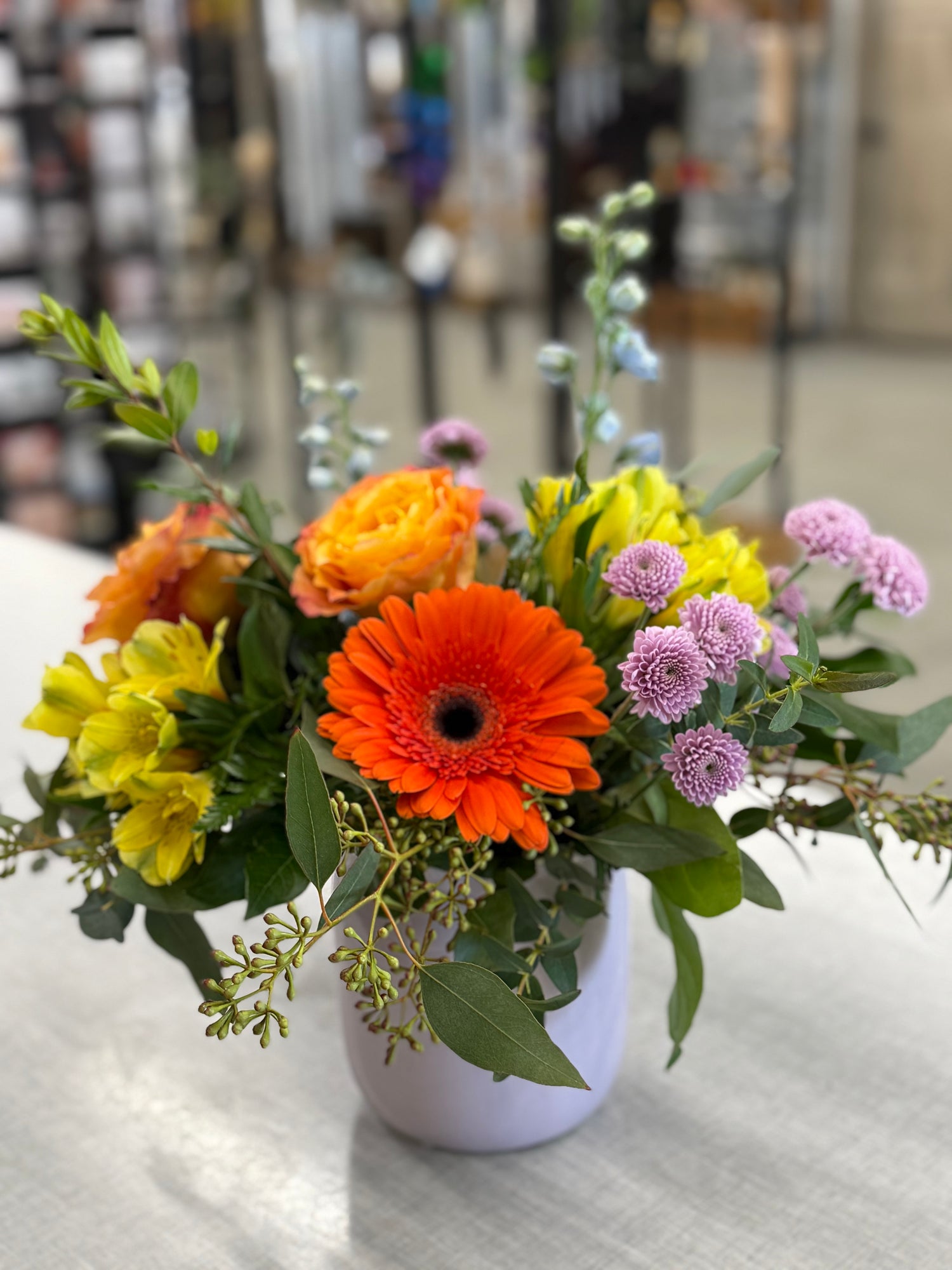 A vibrant bouquet of fresh-cut flowers, including orange, yellow, and purple flowers, arranged in a white container.