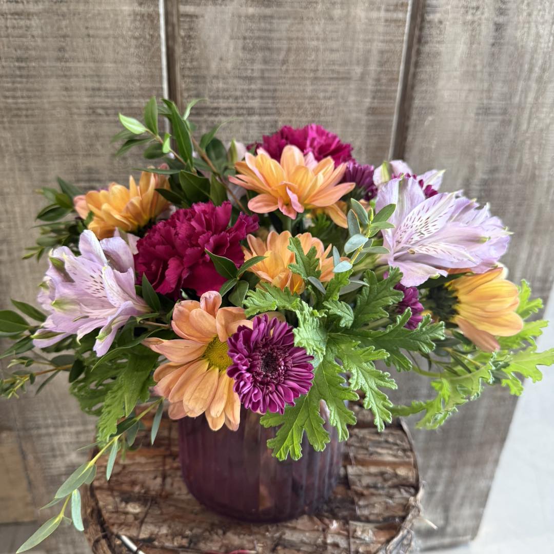 Bouquet of colorful flowers in a purple glass vase.