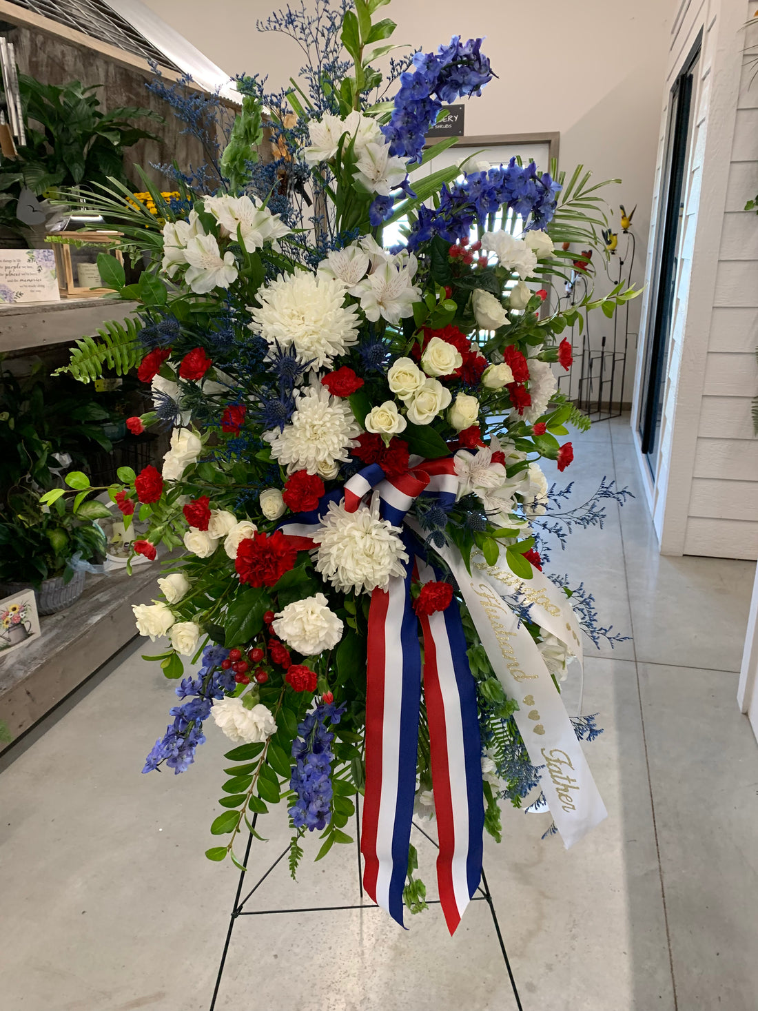 Americana funeral easel spray featuring red, white, and blue flowers with fresh greenery.
