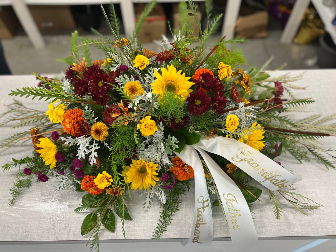 A floral casket spray with a variety of flowers including red, yellow, and white colors, arranged on a table.